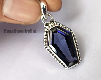 May include: A silver pendant featuring a dark blue gemstone in a coffin-shaped setting. The pendant has a detailed border with small beads.