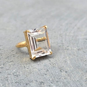 May include: A gold ring featuring a large, clear, square-shaped gemstone.