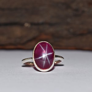 May include: A silver ring with a red star ruby gemstone.