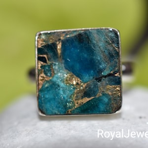May include: A square-shaped ring with a blue and gold gemstone. The gemstone is made of many small pieces of blue and gold material.