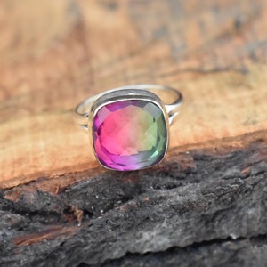 May include: A silver ring with a square-shaped, multi-colored gemstone. The gemstone is a gradient of pink, green, and purple.