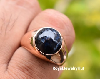 Puede incluir: Un anillo de oro con una gran piedra preciosa redonda de color azul oscuro. La piedra preciosa tiene un efecto brillante e iridiscente.