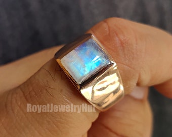 Puede incluir: Un anillo de plata con una piedra de luna de forma cuadrada engastada en el centro. El anillo tiene una banda texturizada.
