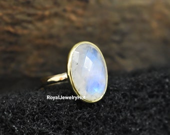 Puede incluir: Un anillo de oro con una gran piedra de luna ovalada. La piedra de luna tiene un brillo iridiscente blanco y azul.