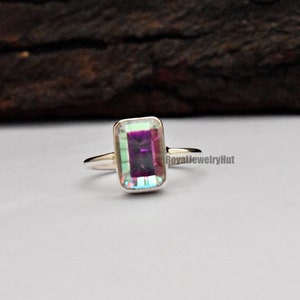 May include: A silver ring with a rectangular, iridescent gemstone. The gemstone has a purple hue with green and blue flashes.