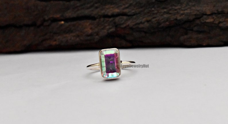 May include: A silver ring with a rectangular, iridescent gemstone. The gemstone has a purple hue with green and blue flashes.