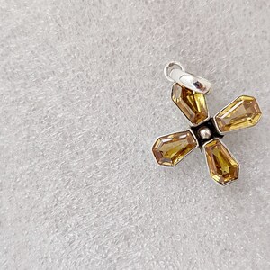 May include: A silver charm with a four-pointed star design featuring yellow gemstones.