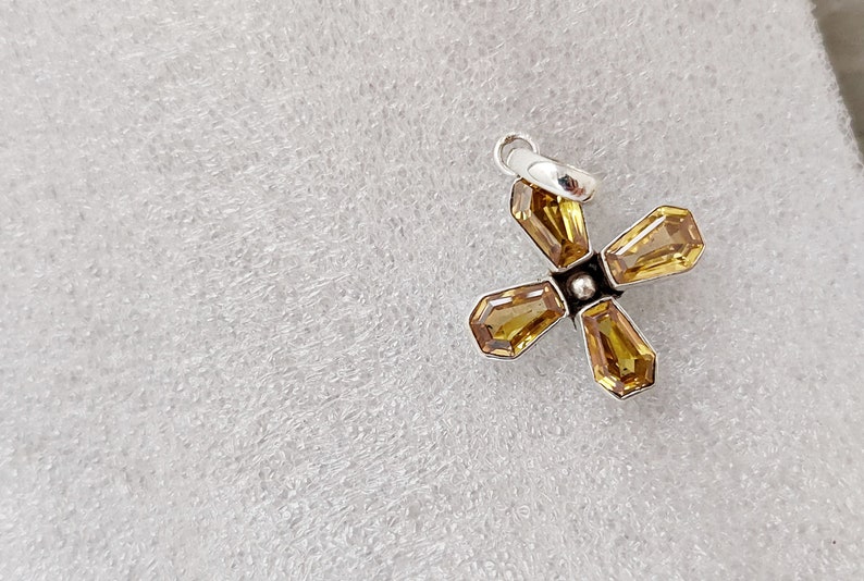May include: A silver charm with a four-pointed star design featuring yellow gemstones.