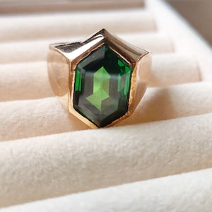Puede incluir: Un anillo de oro con una gran piedra preciosa verde facetada engastada en una forma hexagonal.