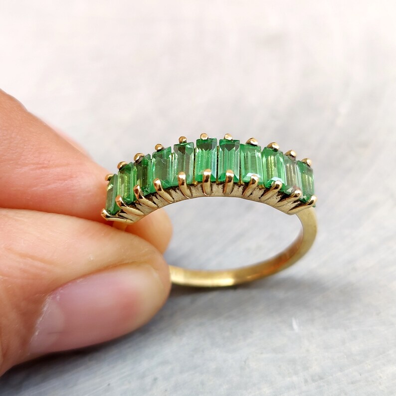 May include: A gold band ring with a row of emerald green baguette-shaped stones.