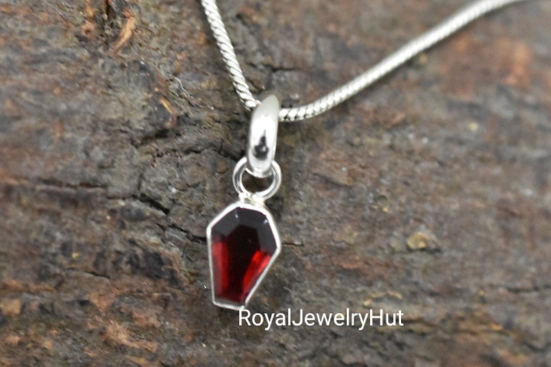 Op de afbeelding: Een zilveren ketting met een klein rood edelsteen kistje hanger.