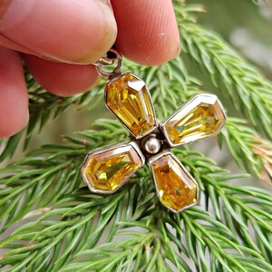 May include: A silver pendant with a flower design featuring four yellow gemstones.