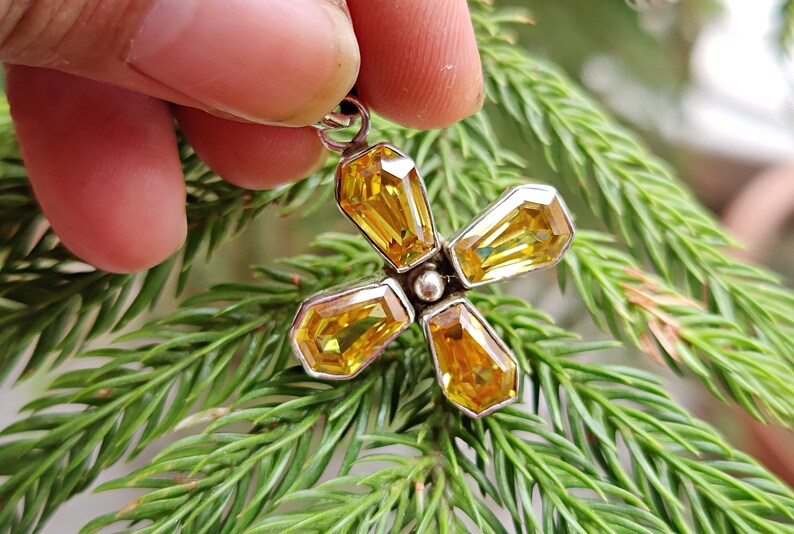 May include: A silver pendant with a flower design featuring four yellow gemstones.