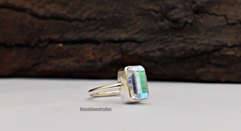 May include: A silver ring with a clear, iridescent rectangular gemstone. The ring is set on a white background.