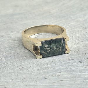 May include: A gold ring with a green and black stone set in a square shape.