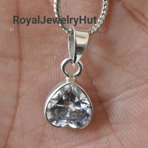 Puede incluir: Un colgante de plata en forma de coraz&oacute;n con una piedra de cristal transparente. El colgante est&aacute; unido a una cadena de plata.