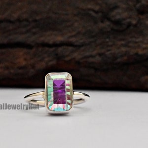 May include: A silver ring with a rectangular iridescent gemstone. The gemstone has a purple hue with green and blue flashes.