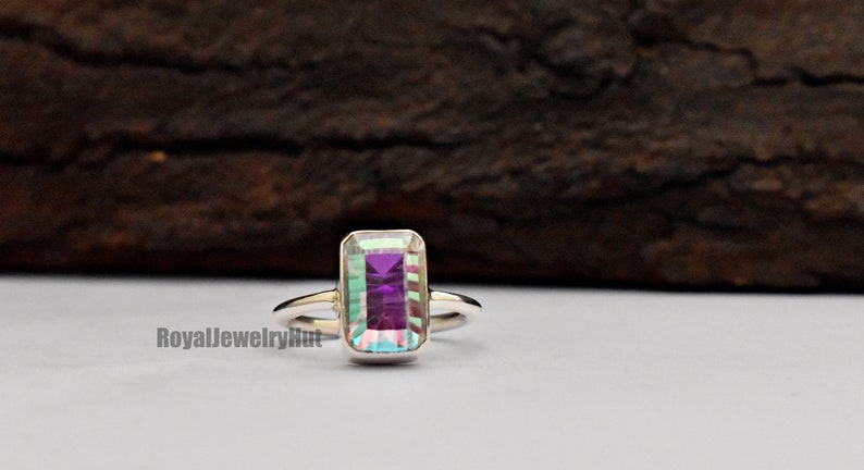 May include: A silver ring with a rectangular iridescent gemstone. The gemstone has a purple hue with green and blue flashes.