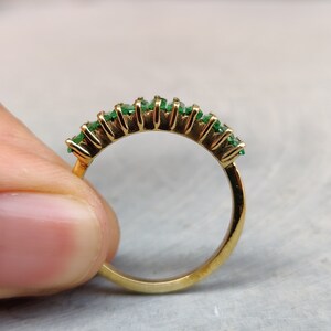 May include: A gold band ring with a row of emerald green gemstones set in a half-circle shape.