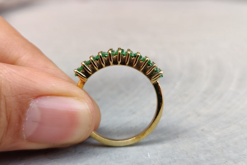 May include: A gold band ring with a row of emerald green gemstones set in a half-circle shape.