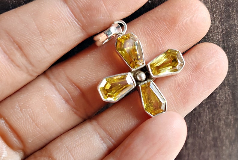 May include: A silver pendant featuring a flower design with five yellow gemstones. The pendant is made of sterling silver and has a polished finish.
