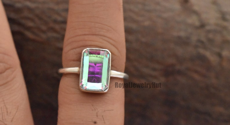 May include: A silver ring with a rectangular iridescent gemstone. The gemstone has a purple, green, and blue color.