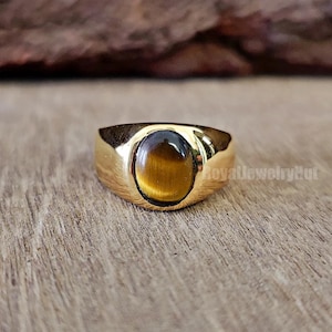 May include: A gold ring featuring an oval tiger's eye gemstone.