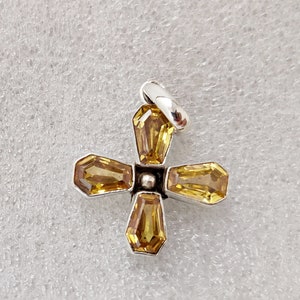 May include: A silver cross pendant with four yellow gemstones. The cross is made of metal and has a simple design.