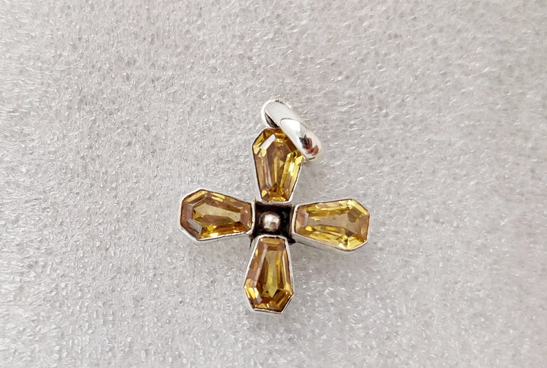 May include: A silver cross pendant with four yellow gemstones. The cross is made of metal and has a simple design.