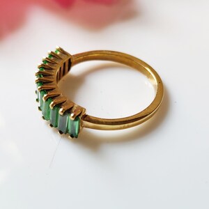 May include: A gold band ring with a row of emerald green baguette-shaped stones.