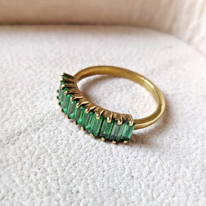 May include: A gold ring with a row of emerald green baguette-shaped stones.