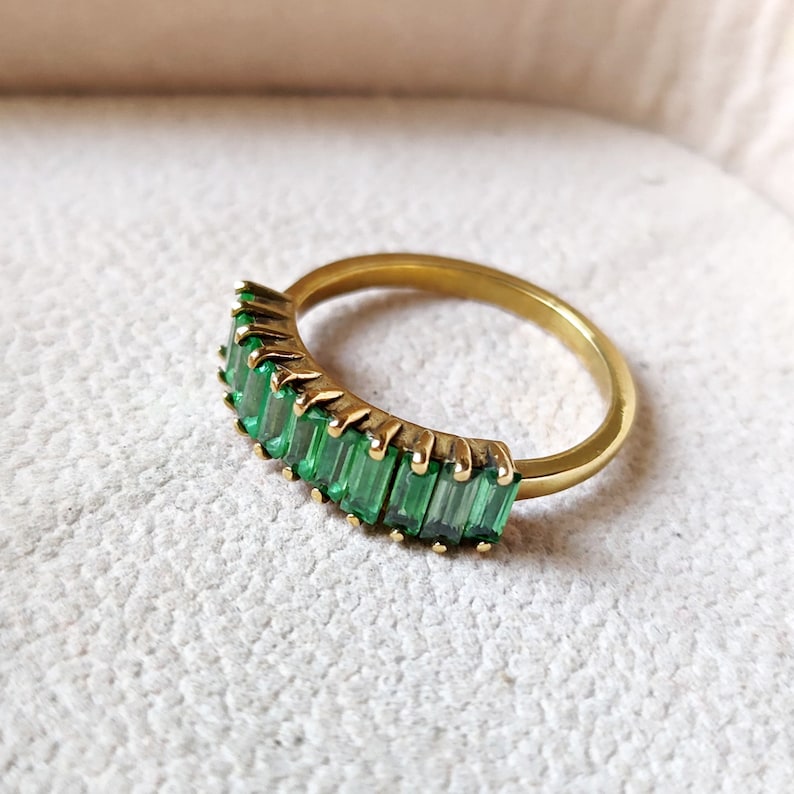 May include: A gold ring with a row of emerald green baguette-shaped stones.