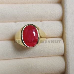 May include: A gold ring with a large, oval-shaped, red gemstone. The ring is set in a simple, classic style.