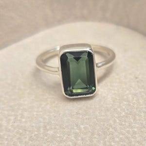 以下が含まれることがあります： 濃い緑色のエメラルドカットの宝石がついたシルバーリング