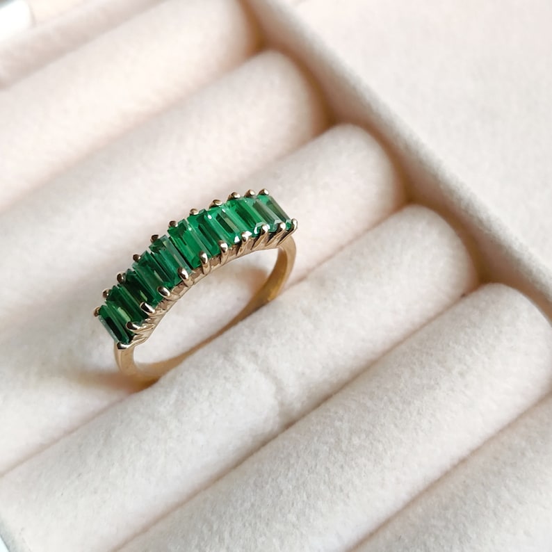 May include: A gold ring with a row of emerald green baguette-shaped stones set in a delicate band.