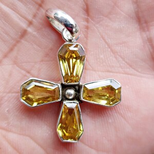 May include: A silver cross pendant with five yellow gemstones. The cross is made of sterling silver and the gemstones are set in a bezel setting.