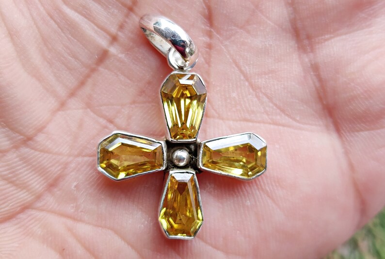 May include: A silver cross pendant with five yellow gemstones. The cross is made of sterling silver and the gemstones are set in a bezel setting.