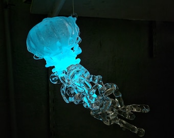May include: A glass sculpture of a jellyfish, with a blue glow emanating from the center of the body. The sculpture is suspended from the ceiling.