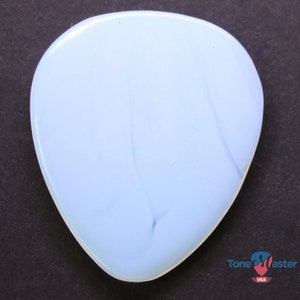 May include: A pale blue guitar plectrum with a pearlescent sheen. The pick has a rounded triangular form and a smooth surface. Subtle white and blue marbling adds visual interest. The Tone Master USA logo is visible in the bottom right corner.