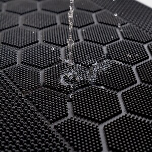 May include: Close-up of a black rubber mat with a hexagonal pattern of small raised dots. Water is dripping onto the mat, creating a small splash.