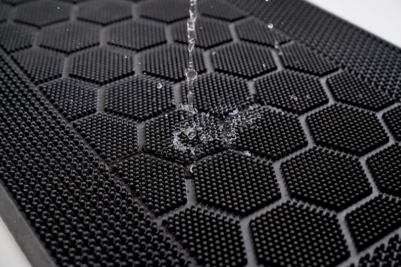 May include: Close-up of a black rubber mat with a hexagonal pattern of small raised dots. Water is dripping onto the mat, creating a small splash.
