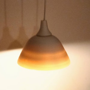 Könnte beinhalten: Ein weißer und beiger Lampenschirm mit schlichtem Design hängt an einem weißen Kabel.