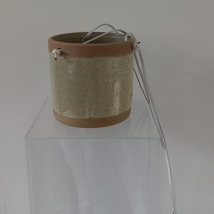 May include: A light brown ceramic hanging planter with a light green glaze and white string hanging loops.