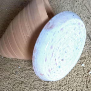 May include: A white ceramic planter with a pink and white speckled glaze. The planter is shaped like a cone and has a wide opening at the top.