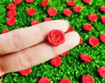 May include: A single red fabric rose held in a hand against a green background of many other red fabric roses.