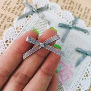 Peut inclure: Gros plan sur une main tenant un petit nœud gris. Le nœud est fait d'un matériau doux et velouté et a un design simple et élégant.
