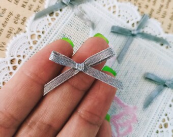 Puede incluir: Primer plano de una mano sosteniendo un pequeño lazo gris. El lazo está hecho de un material suave y aterciopelado y tiene un diseño simple y elegante.