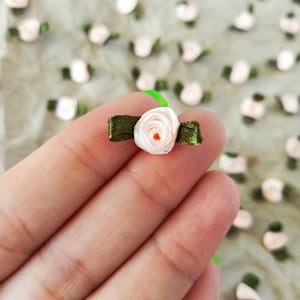 May include: A close-up of a single, small, light pink satin rose with a green ribbon bow. The rose is held in a hand.