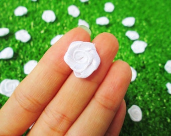 Könnte beinhalten: Nahaufnahme einer weißen Stoffrose, die in einer Hand gehalten wird. Die Rose ist klein und zart, mit einem einfachen Design. Der Hintergrund ist eine grüne Grasfläche.