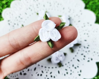 Könnte beinhalten: Nahaufnahme einer weißen Stoffblume mit grünen Blättern. Die Blume besteht aus drei Stoffschichten und wird von einem Finger gehalten.